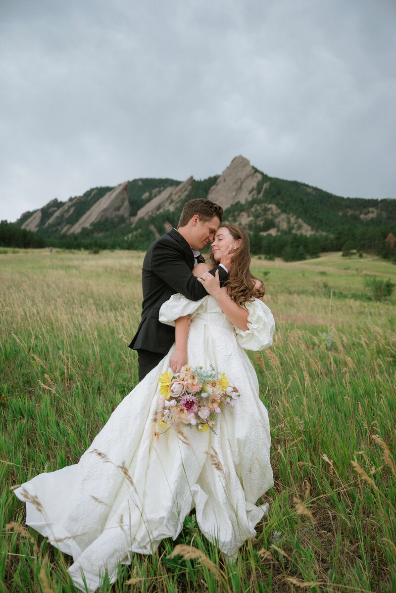 Groom chasing Bride through grassy field with mountains behind them