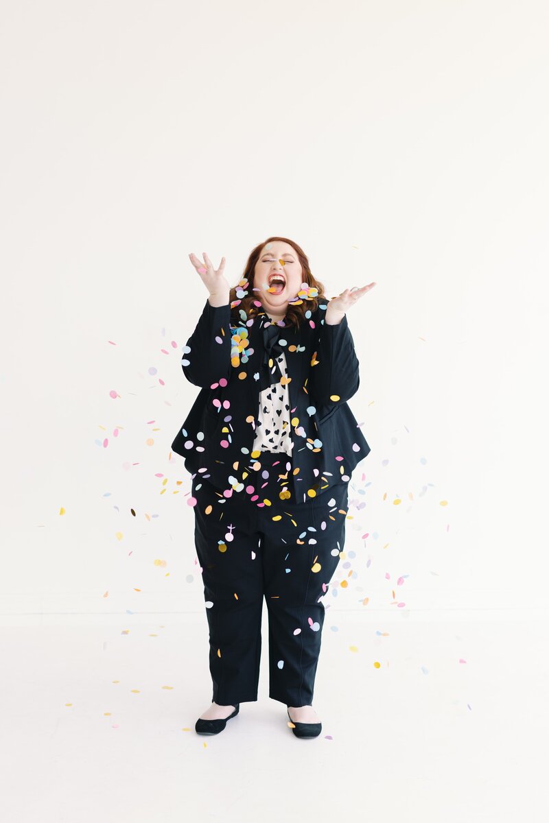 woman in black suit throwing confetti and laughing