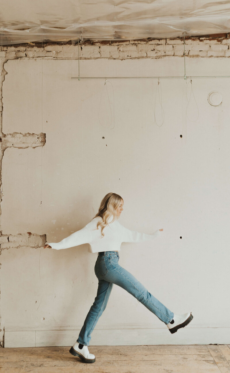 Colorado Studio Portrait Session. Jadyn Alexa Films walking and swinging her legs along a white brick wall