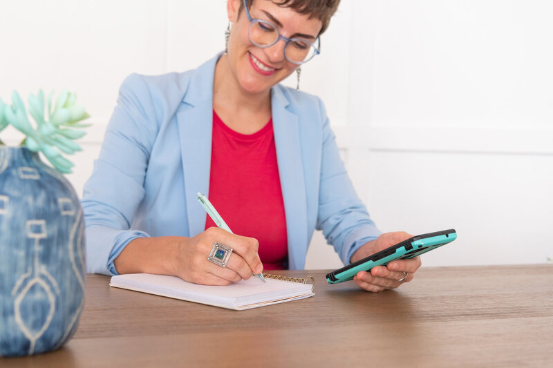 A woman in holding her phone and writing down notes.
