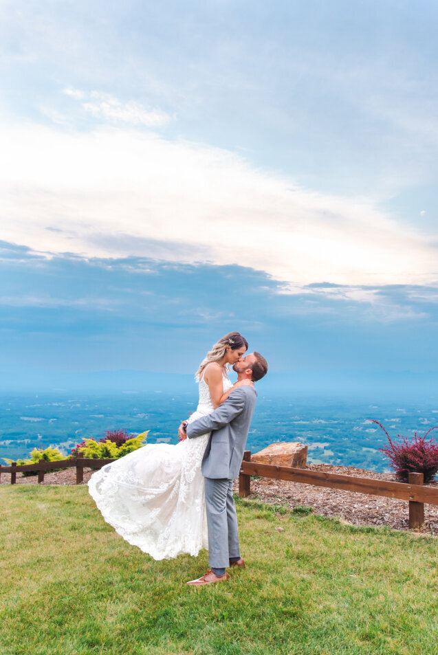 A groom holding and kissing his bride on the grass at Hidden Hill.