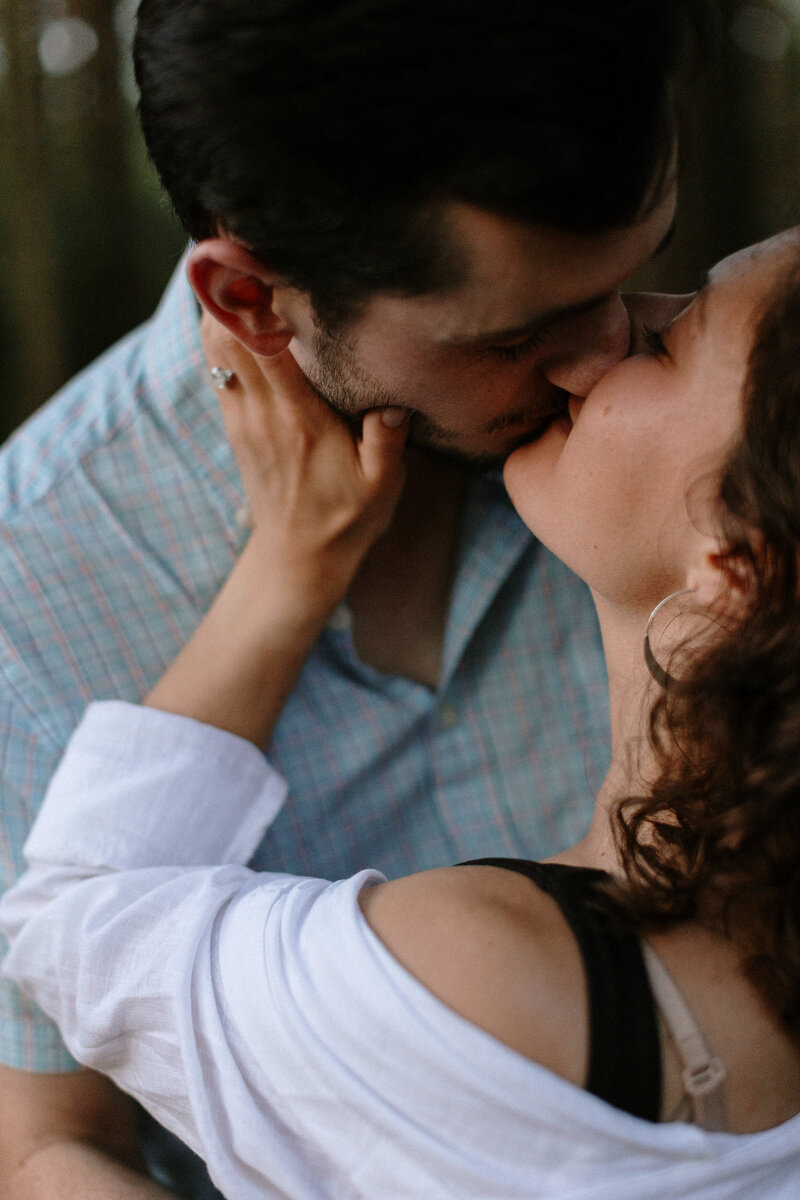 A couple shares an intimate moment, with one partner gently touching the other's face, surrounded by a blurred natural background.