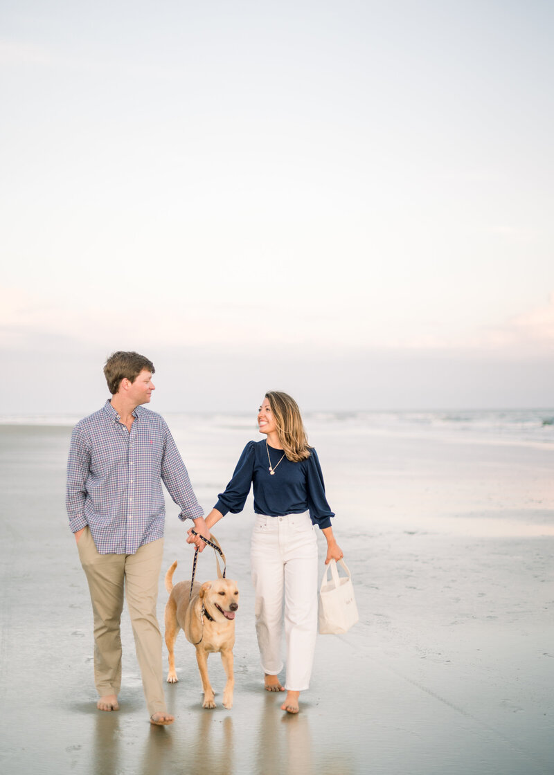 couple walks on the beach with their dog