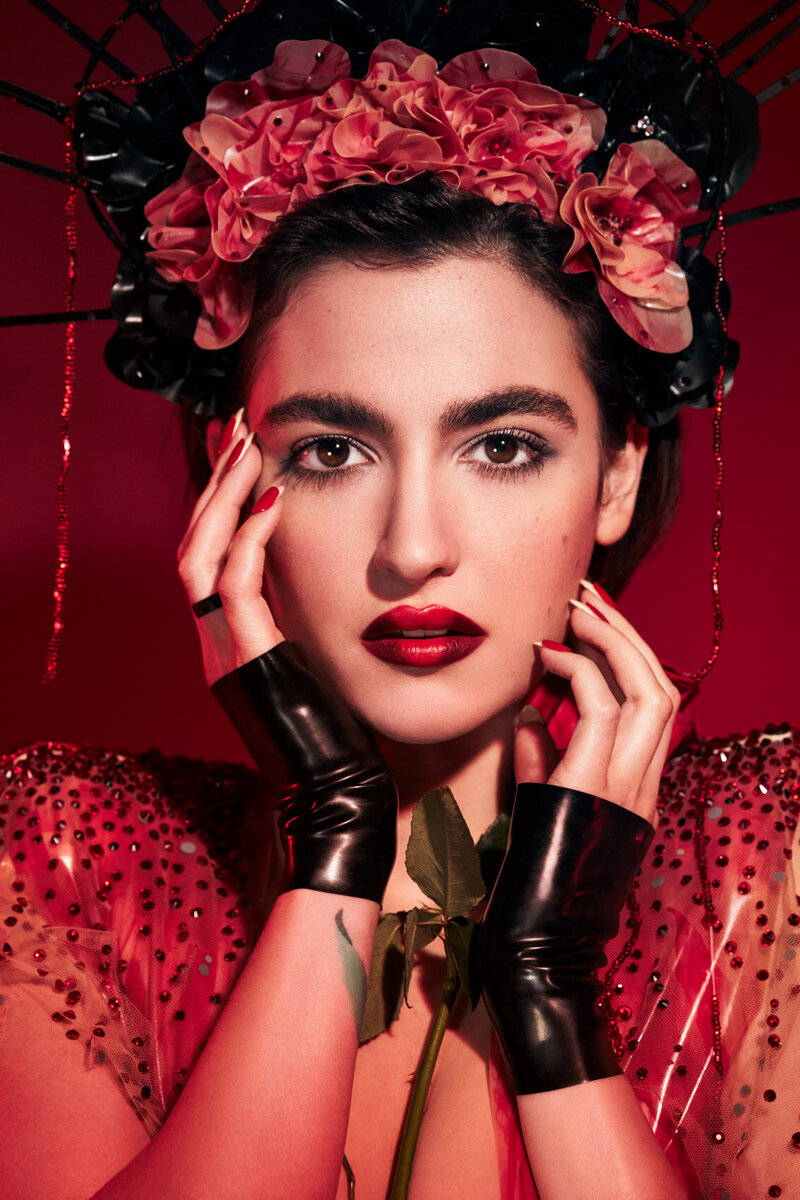 Bold portrait of Hannah Cruz wearing a red floral headpiece and lace outfit, with striking makeup, captured by Ylva Erevall.