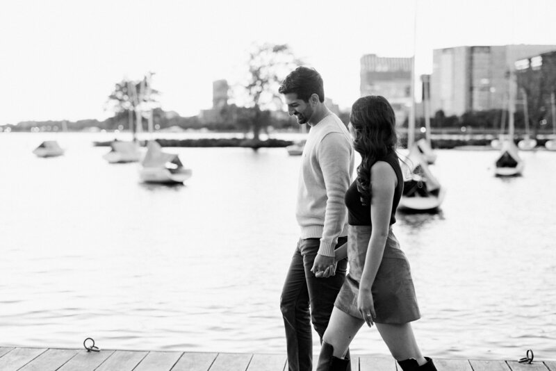 Couple holding hands and walking along a dock next to the water.