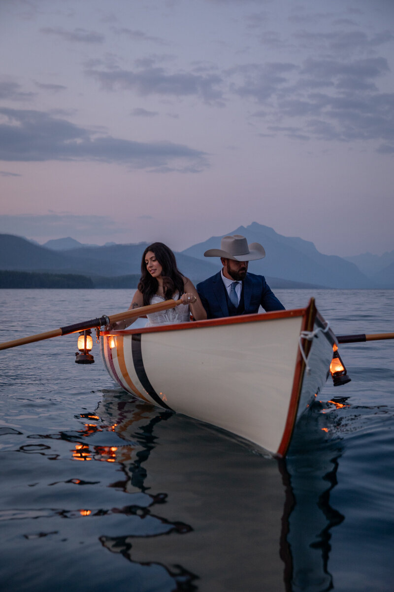 Bride & Groom paddle a canoe at sunset and with lanterns on a lake in Glacier National Park.