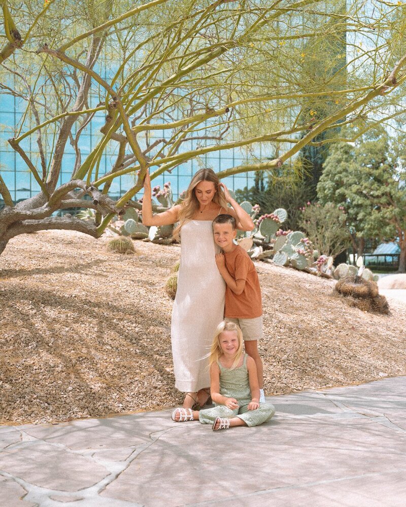 Family portrait in Costa Mesa with mom and two kids under desert trees and cactus garden, blending modern and natural backdrops.