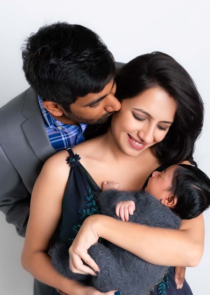 parents-kissing-over-newborn-baby-portrait