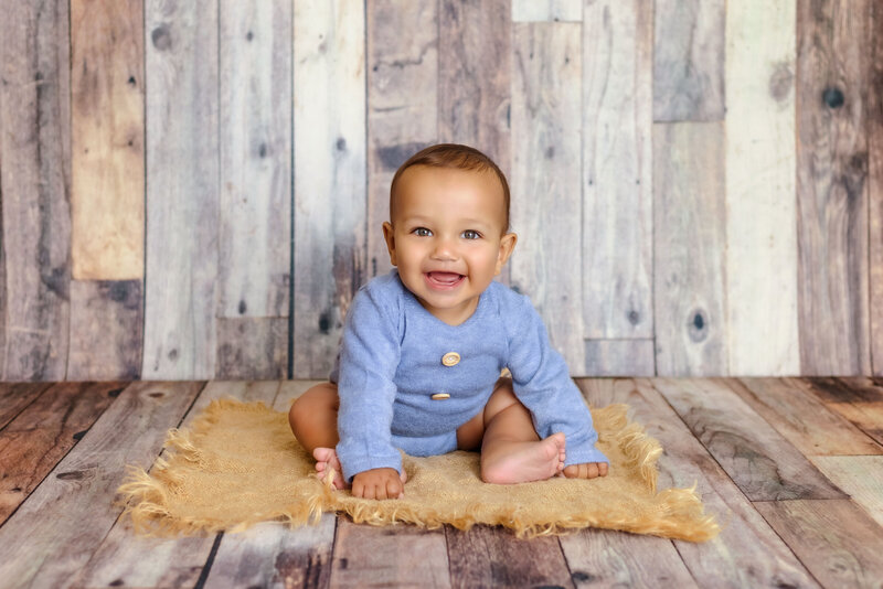 Milestone photographer- a baby sits on a wood floor smiling