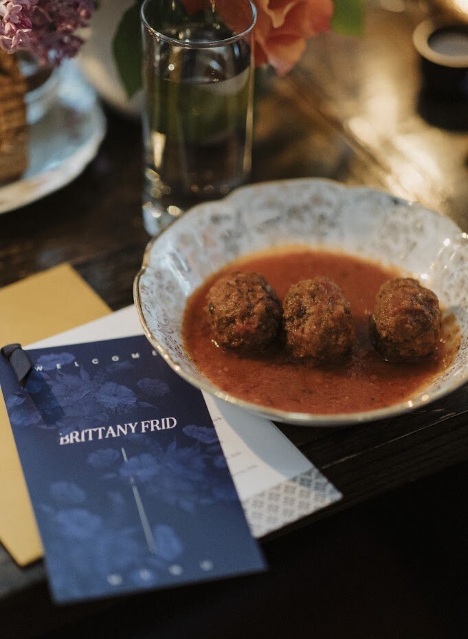 A modern blue multi-page menu sits next to a bowl of polpetta meatballs at a wedding at North & Navy in Ottawa, designed by Frid Events.