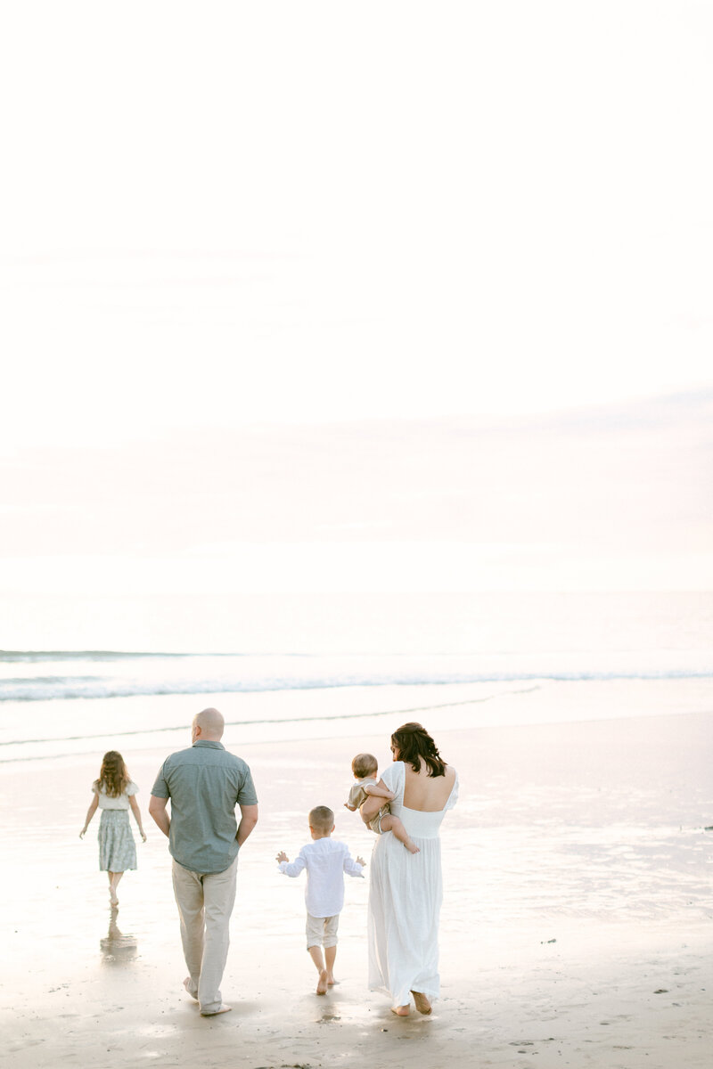 parents and 3 young children walk down the beach at sunset during family photography session