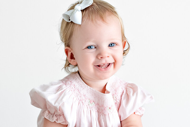 A little girl with blue eyes smiles at the camera during family photos at a studio in Huntsville Alabama