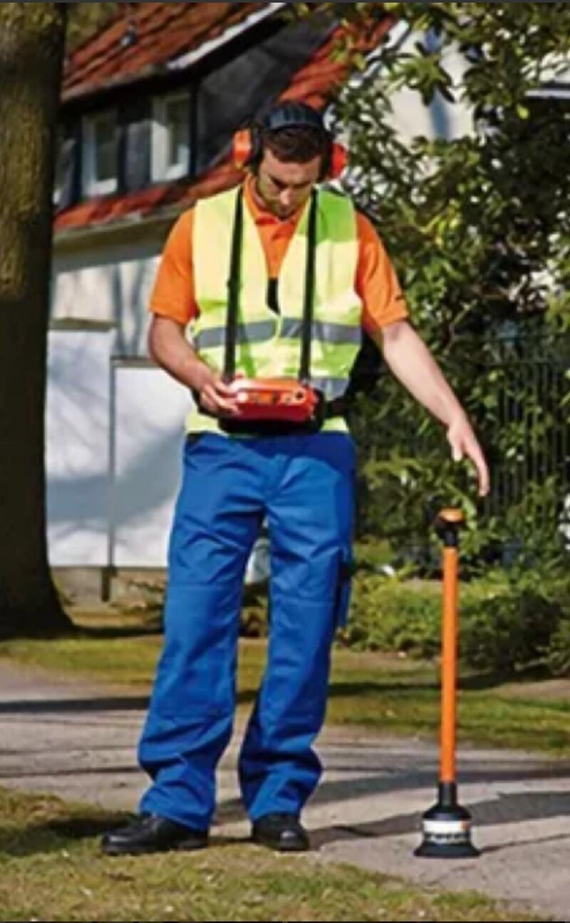 a man in blue pants, orange shirt, and yellow vest monitoring water level with machine