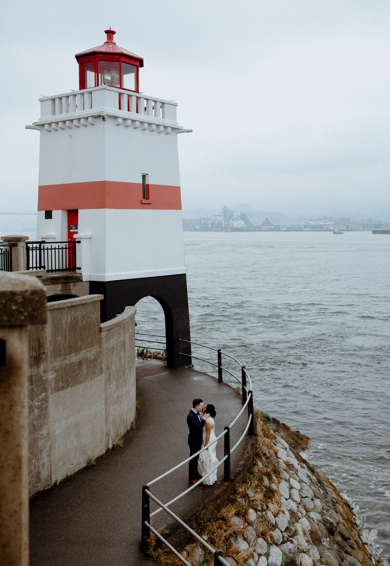 Couple kissing in front of a lighthouse at their Stanley Park Teahouse Wedding