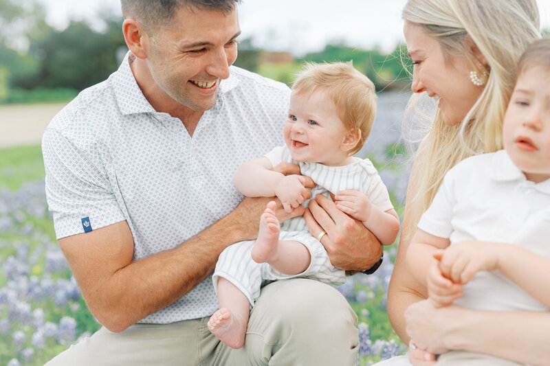 A joyful father holding his smiling baby in a vibrant field of Texas bluebonnets, perfect for spring family photography in Dallas.