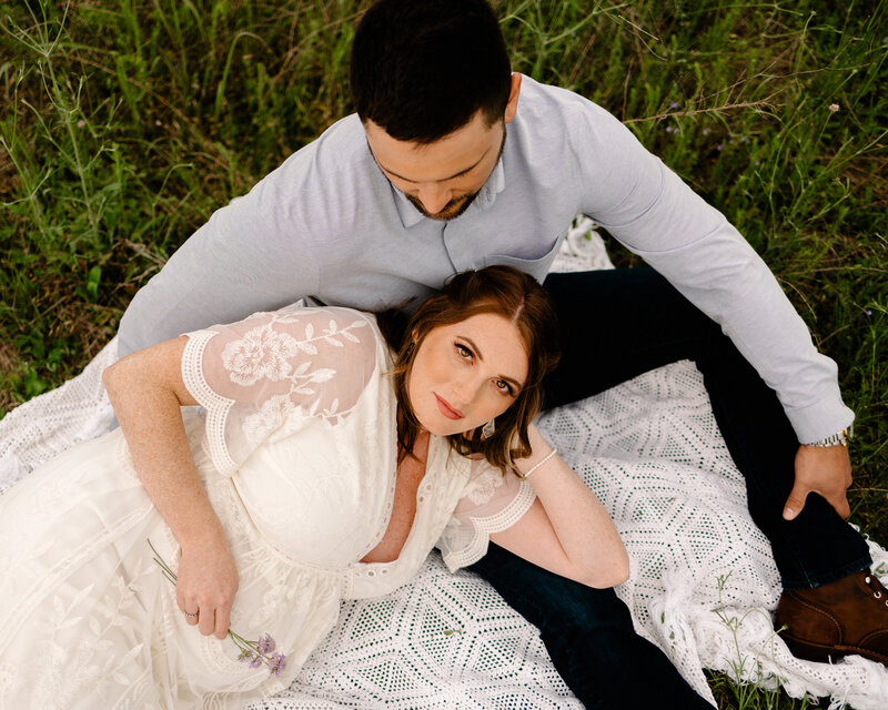 the artistry of a professional family photographer in Albuquerque with this beautiful shot of a couple in the grass. The woman, dressed in a white dress, gazes directly at the camera while the man, wearing a light blue t-shirt, looks down.