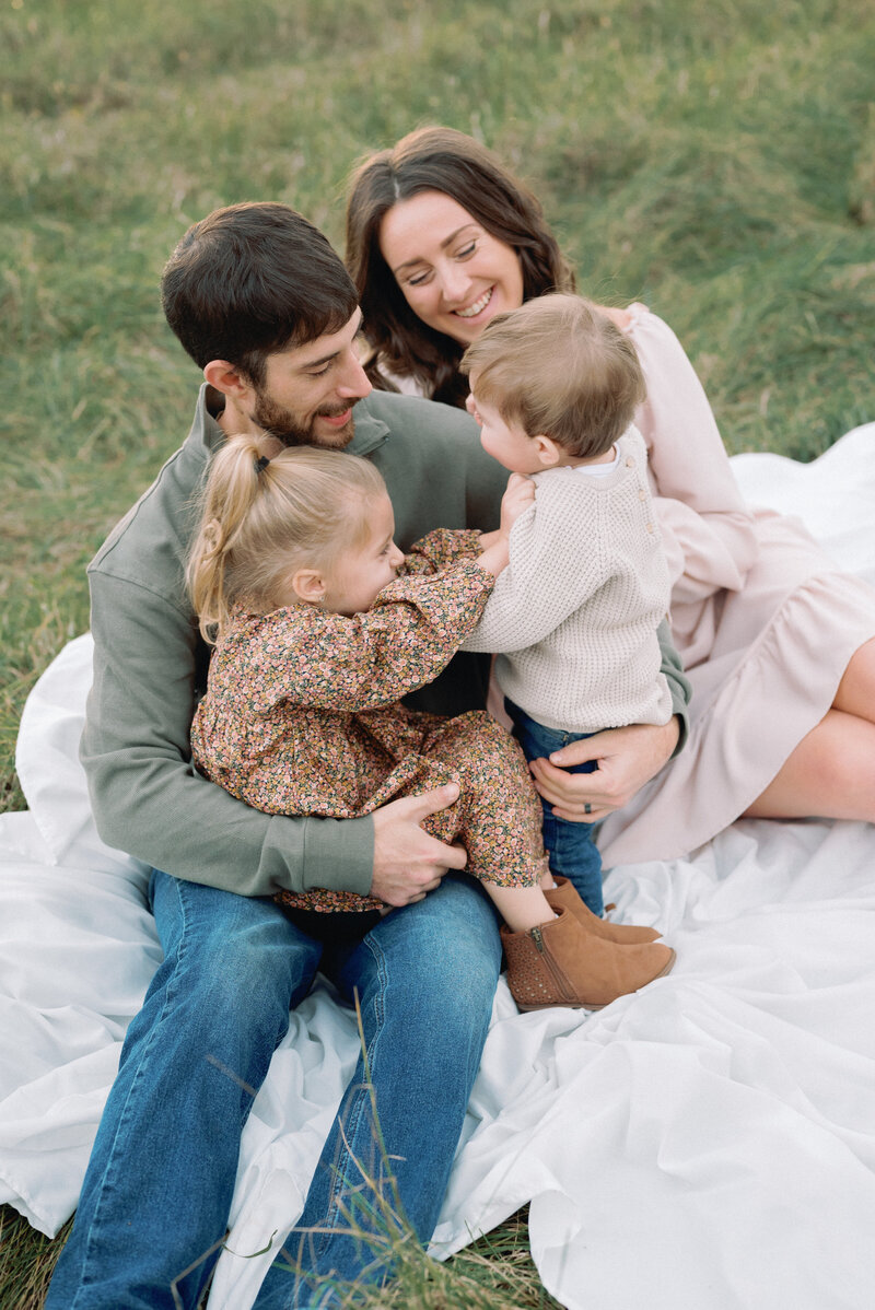 Kids laughing and on their dad's lap in outdoor family photoshoot