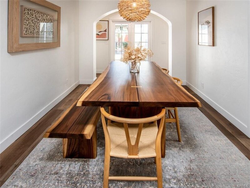 Dining room with natural light, live edge stained wooden table, handcrafted bench, light wood chairs, and rattan chandelier.