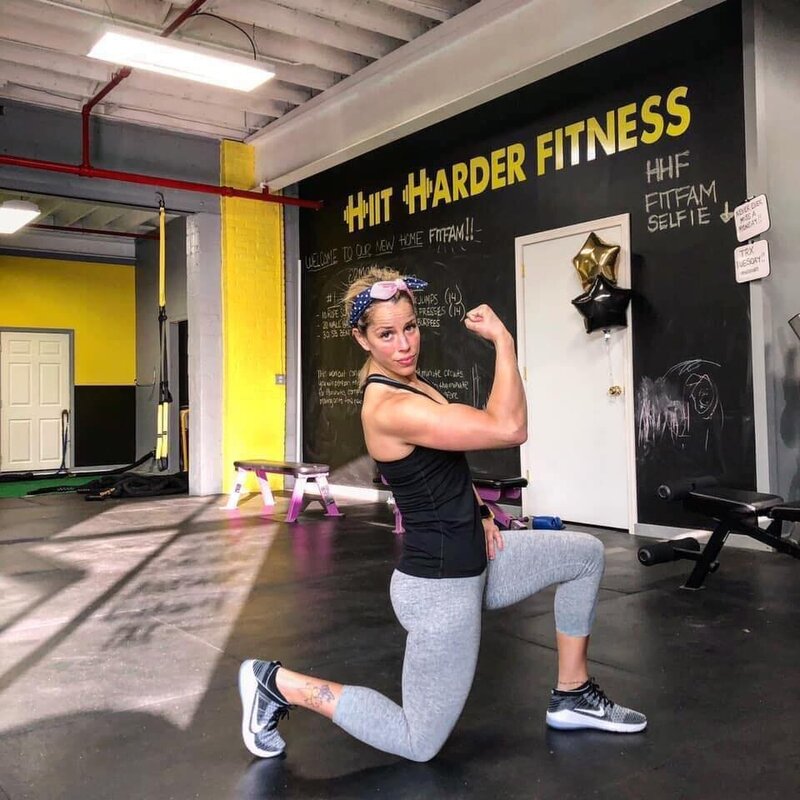 Kim on one knee flexing her arm muscle ready to help people reach their weight loss and fitness goals at a gym called Hiit Harder Fitness