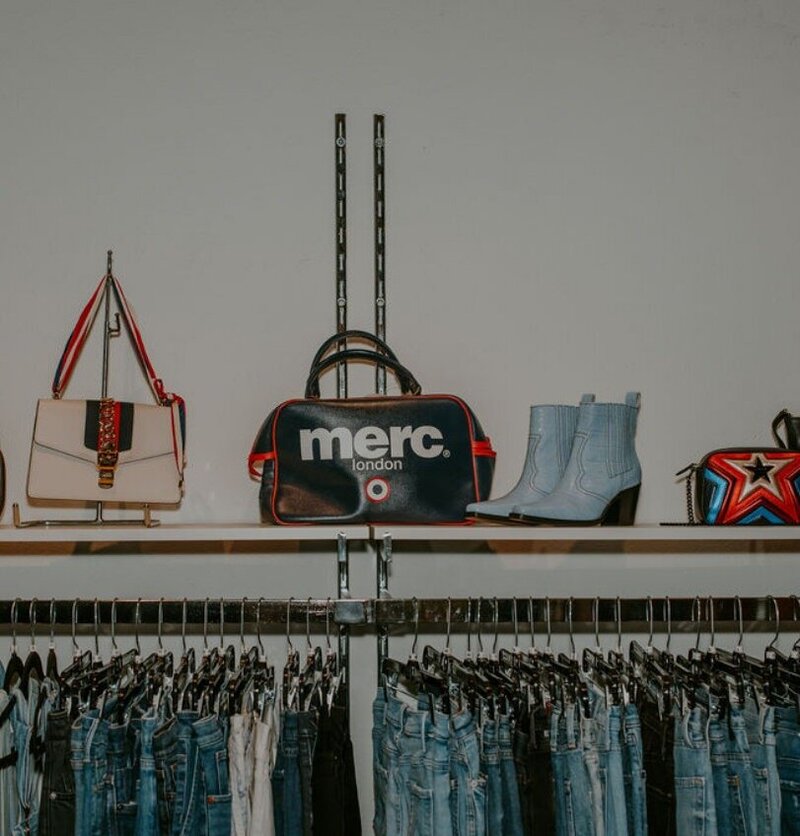 Accessories sitting on top of a shelf over a rack of jeans