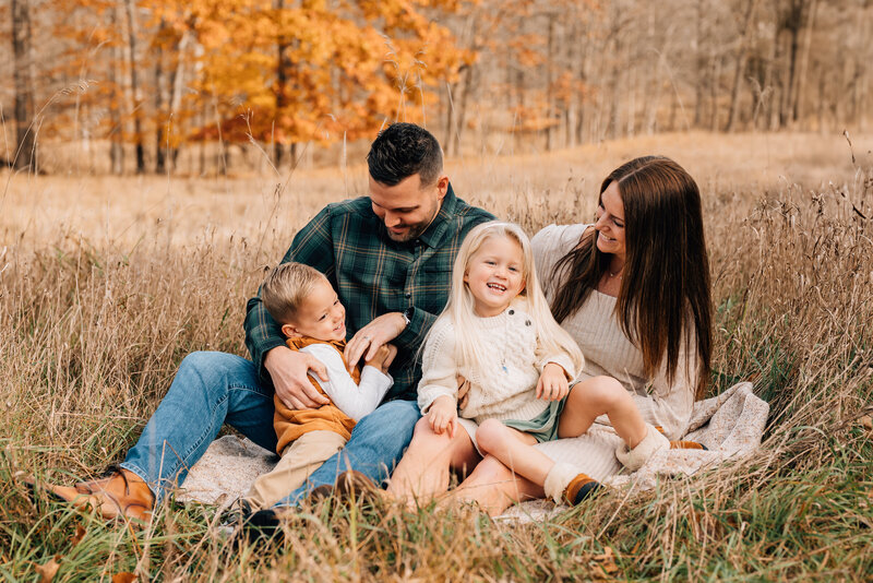 A family with young children playing together in a field of vibrant autumn colored foliage.