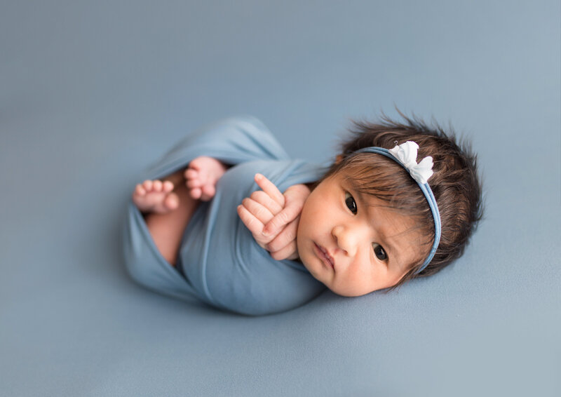 Newborn baby swaddled with headband on blue fabric