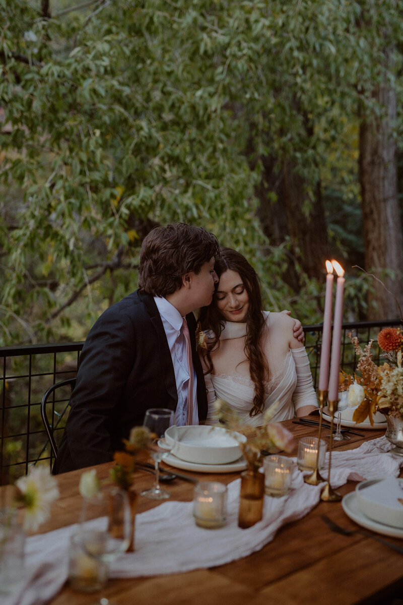 Groom kisses bride as they sit at their table for reception dinner