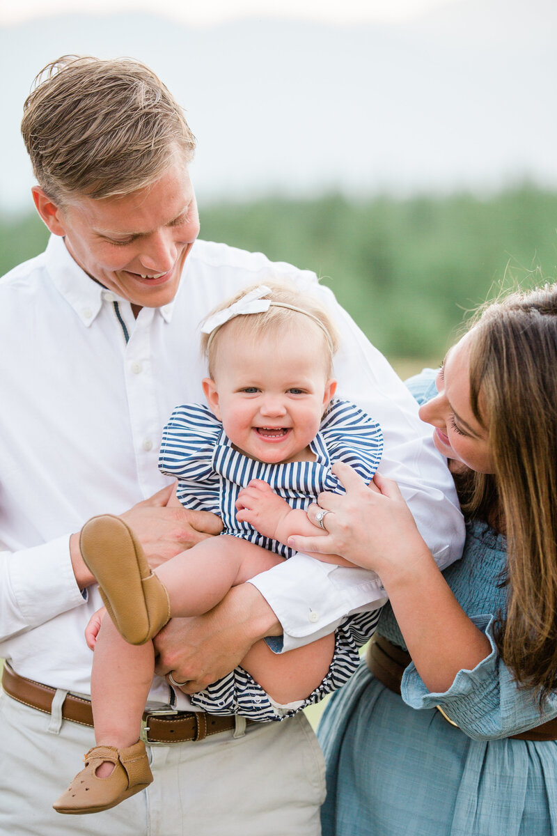 A happy baby sits in dad's arms while mom tickles her captured by a Breckenridge Photographer