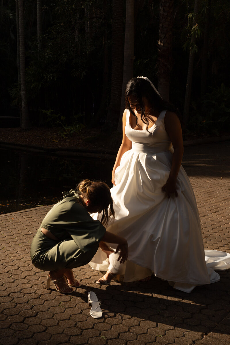 A bride helped by her bridesmaid in Botanical Gardens Brisbane on her wedding day