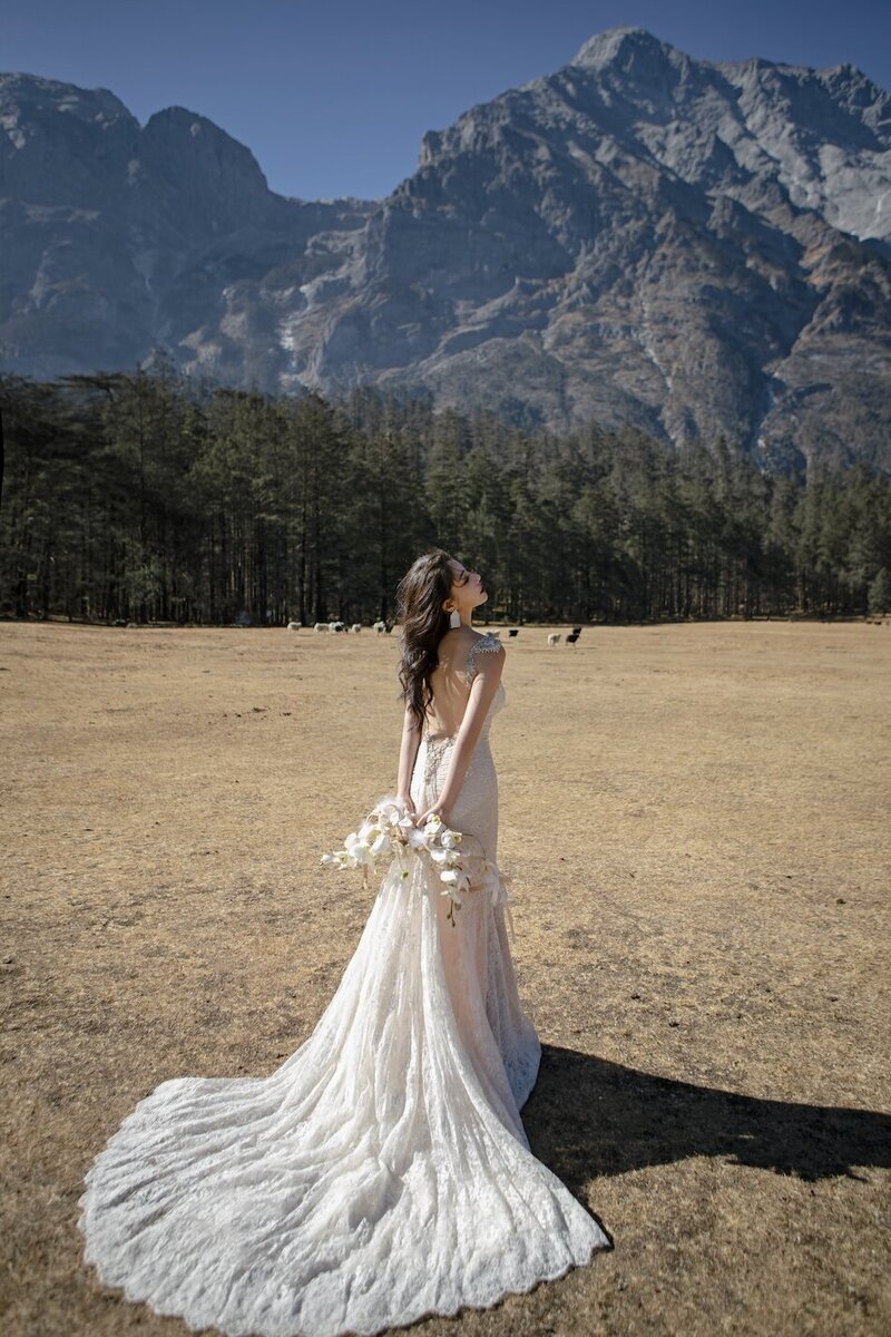 Bride in a couture dress shot in dramatic trees with mountains in the background.