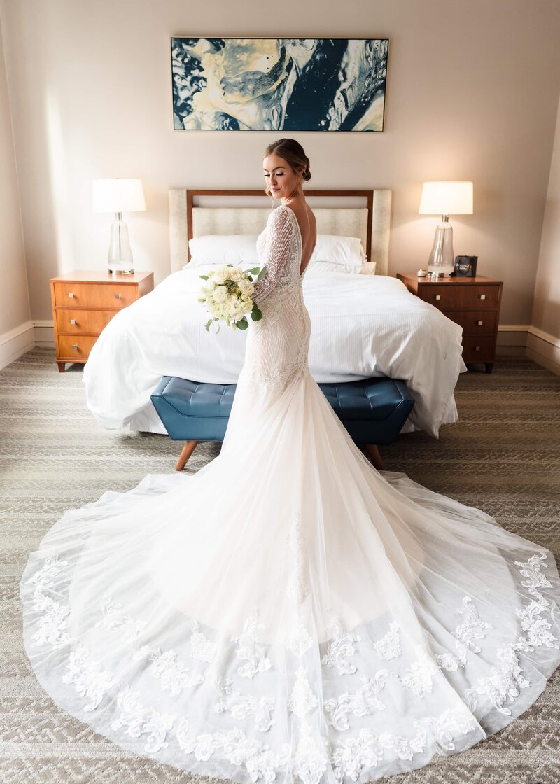 A bride in a white dress with a flowing train looks over her shoulder during bridal portraits in her suite at the Westin Columbus
