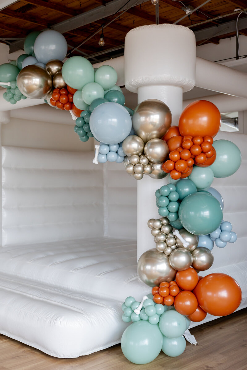Orange, gold, teal balloons with dog bones in a garland on a large white bounce house.