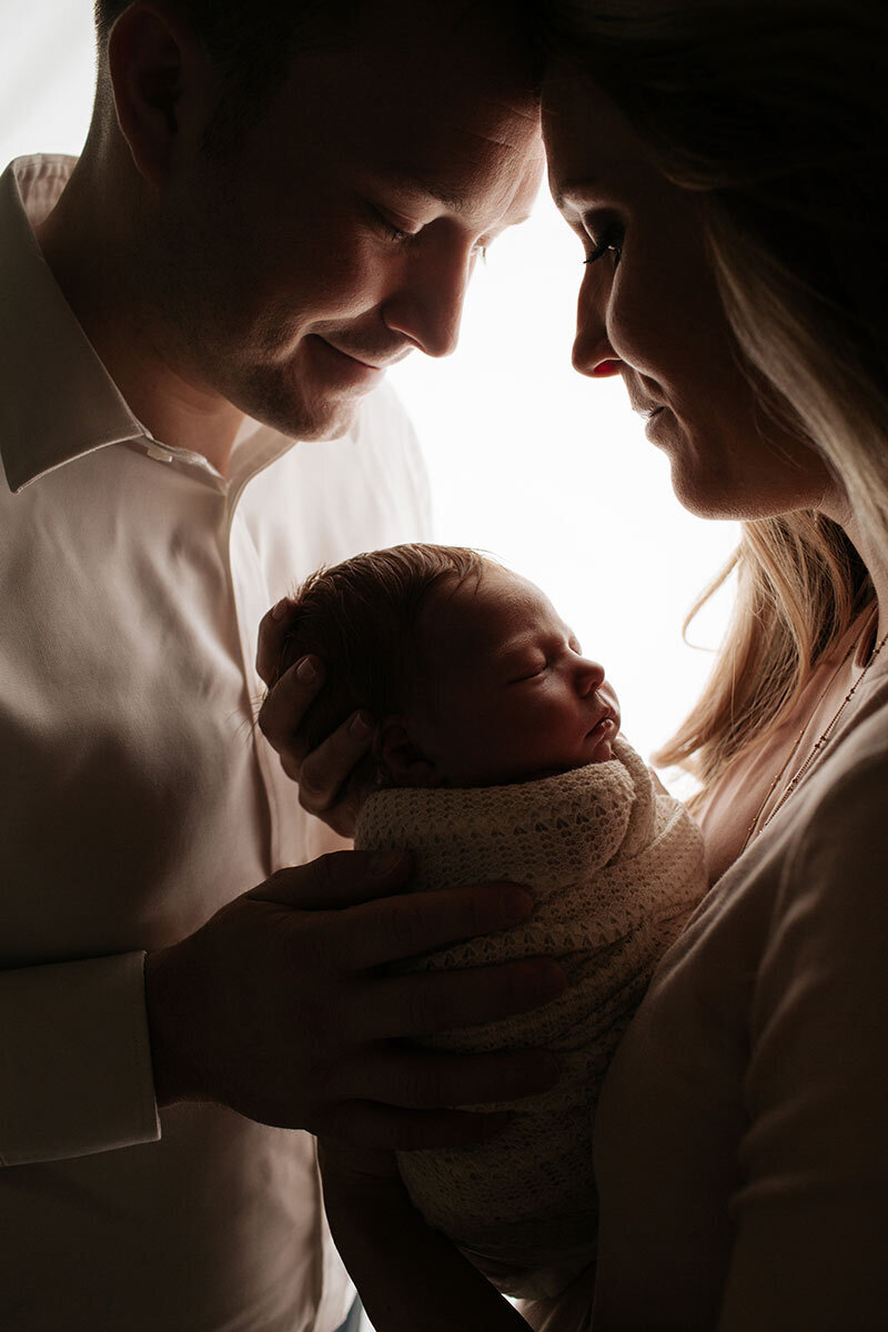 Darkly lit portrait of family looking at newborn