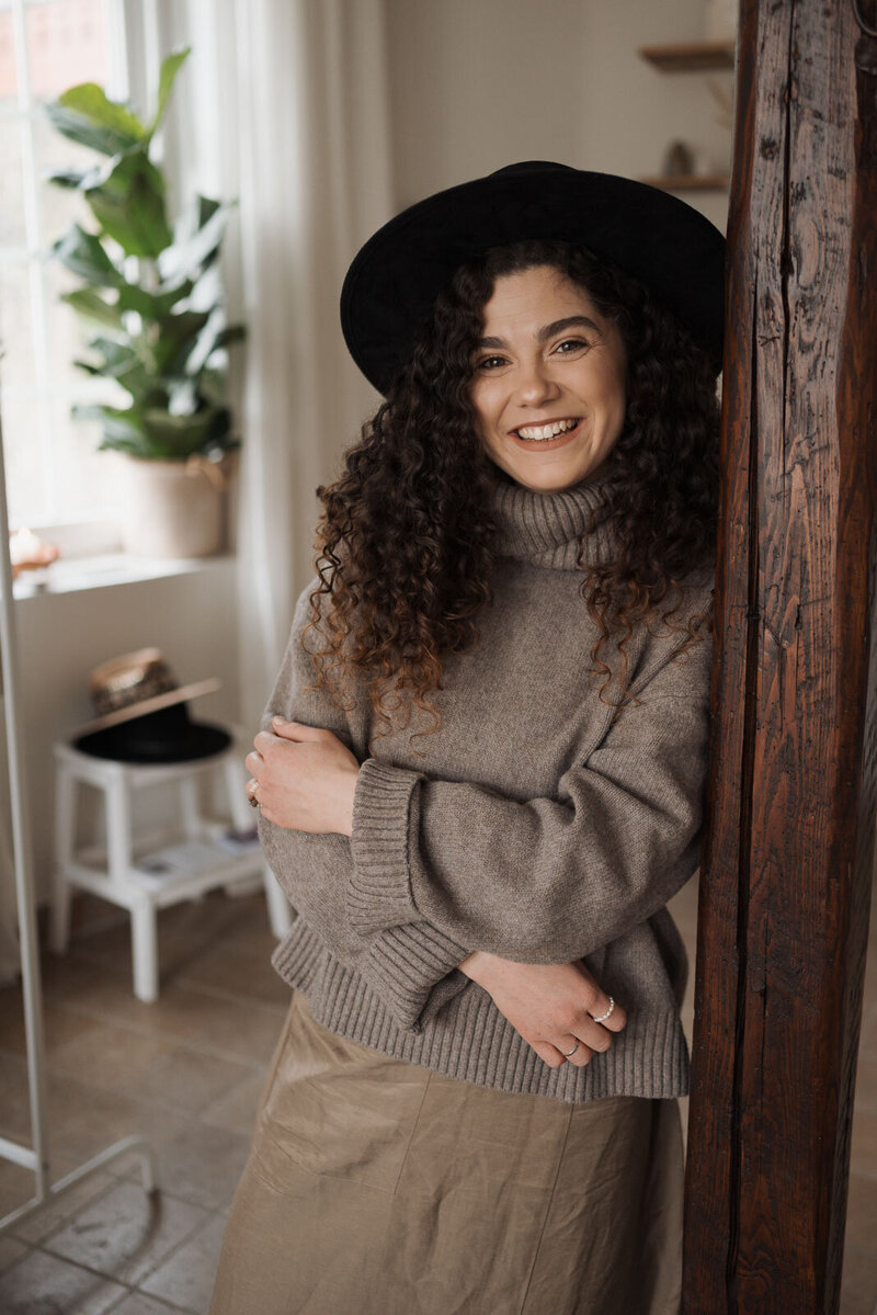 eine lächelnde Frau mit schwarzem Hut in ihrem Schmuckatelier