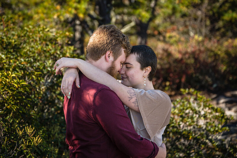 A newly engaged couple wraps their arms around one another and presses their foreheads against one another. They both smile softly and close their eyes as they embrace.