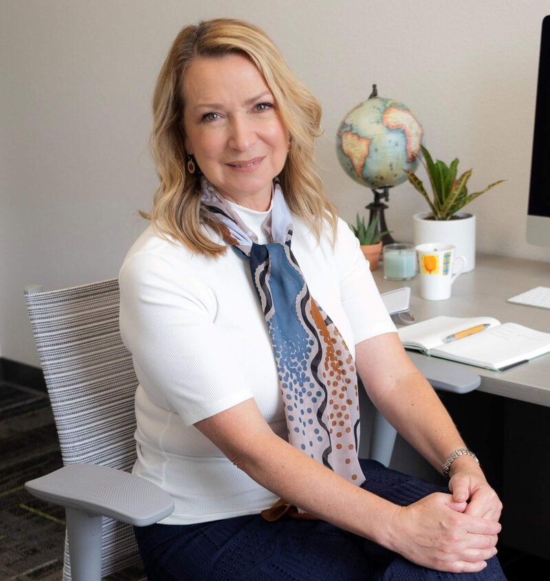 Francine errico owner of Must Writing services sitting  at desk smiling at camera with legs crossed and hands on knee