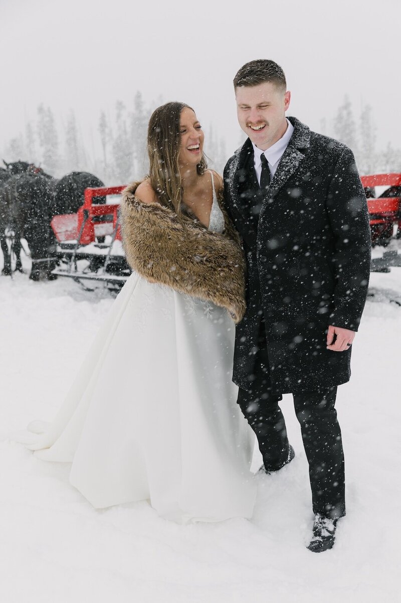 Bride and groom laughing in heavy snowfall during Winter Park micro-wedding — candid Colorado winter wedding moment