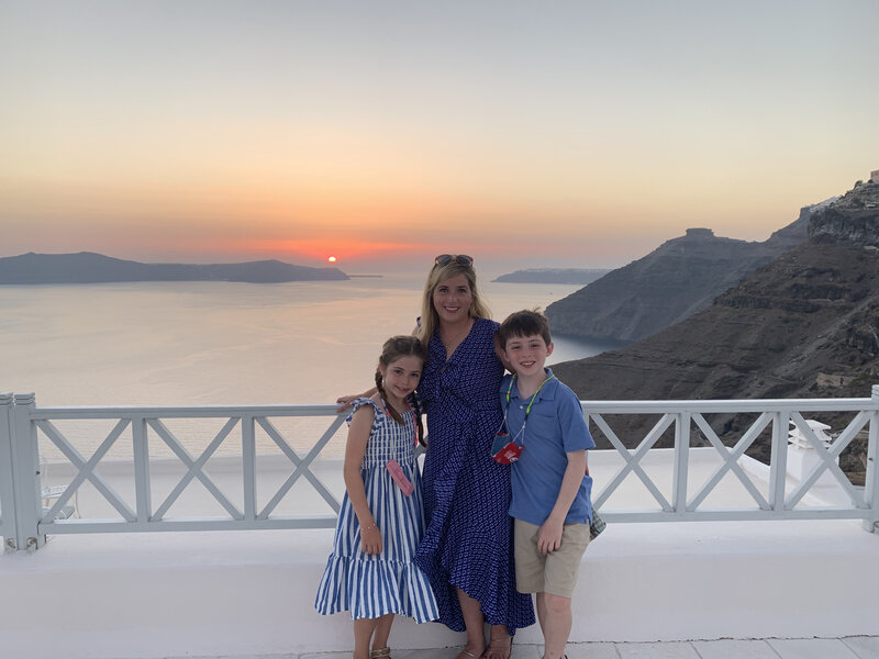 mother and children stand in front of a view of the sunset in santorini greece