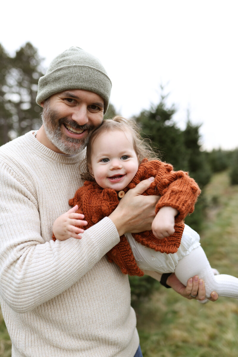 Playful outdoor family session in Maple Grove, Minnesota with parents lifting a blanket while their toddler runs through autumn leaves.