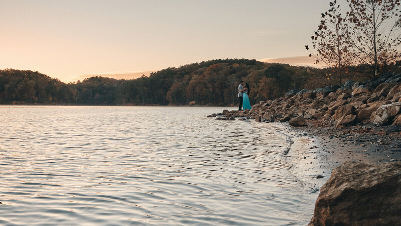 Eloping couple holding each other near the water's edge of a lake