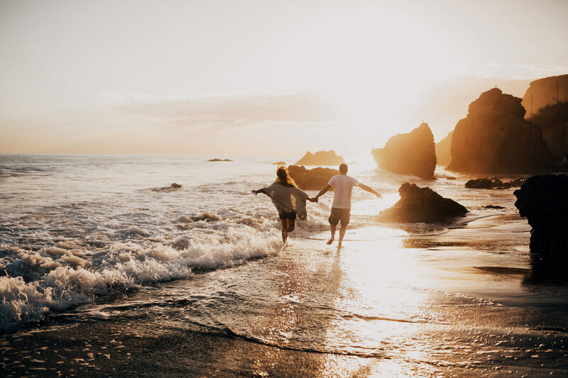 Couple on a beach at sunset running into the water