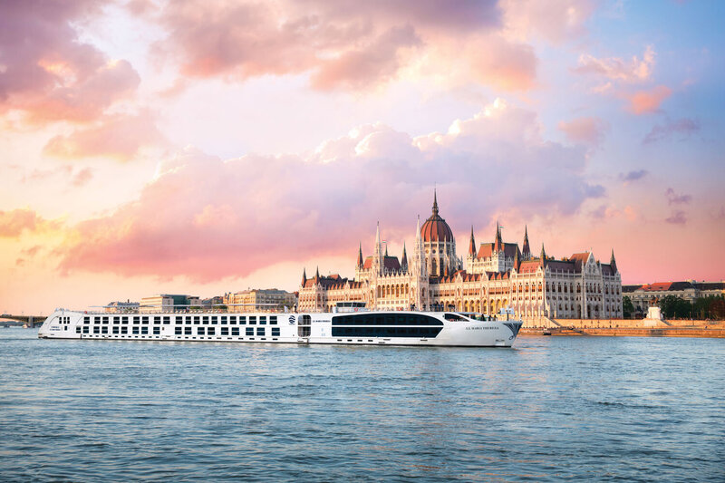 River cruise ship sailing past the Hungarian Parliament Building on the Danube River at sunset.