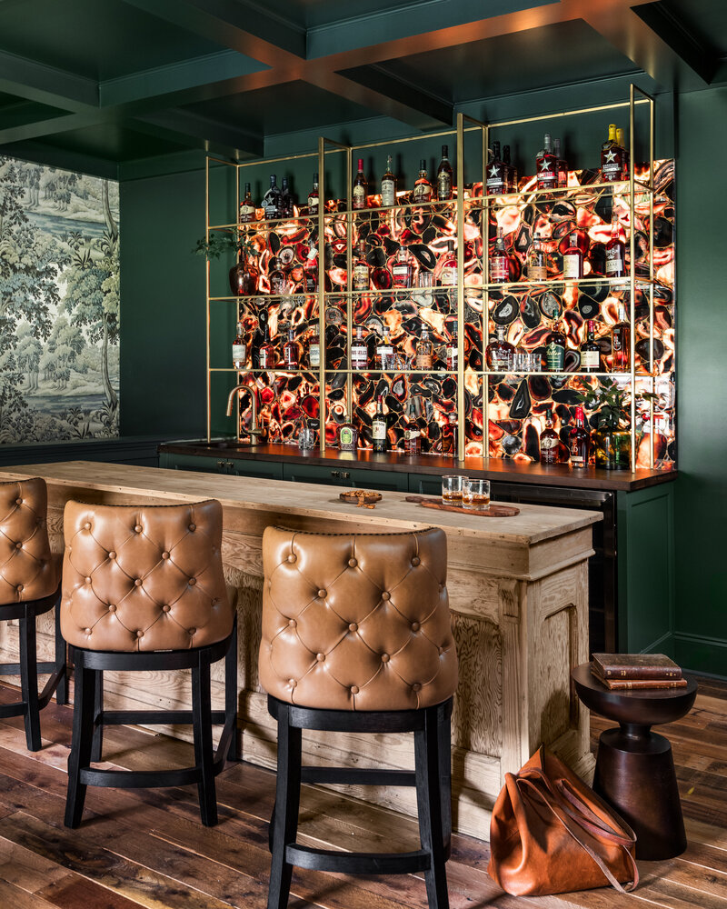 Stylish Irish pub-inspired home bar with tufted leather stools, rich green walls, and a statement liquor display.