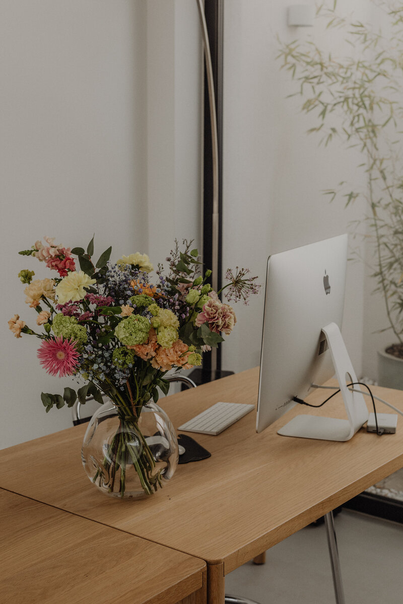 Modern office desk with a computer, notebooks, and a bouquet of flowers — styled workspace photo for The Veiled Method™ Bio Boss™ sales page.