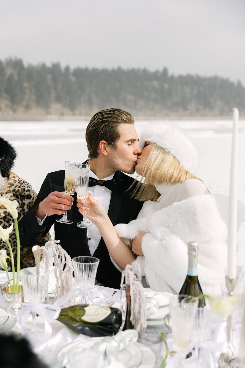 Bride and groom sharing a champagne toast at an outdoor winter wedding tablescape in Colorado at Evergreen Lake House.