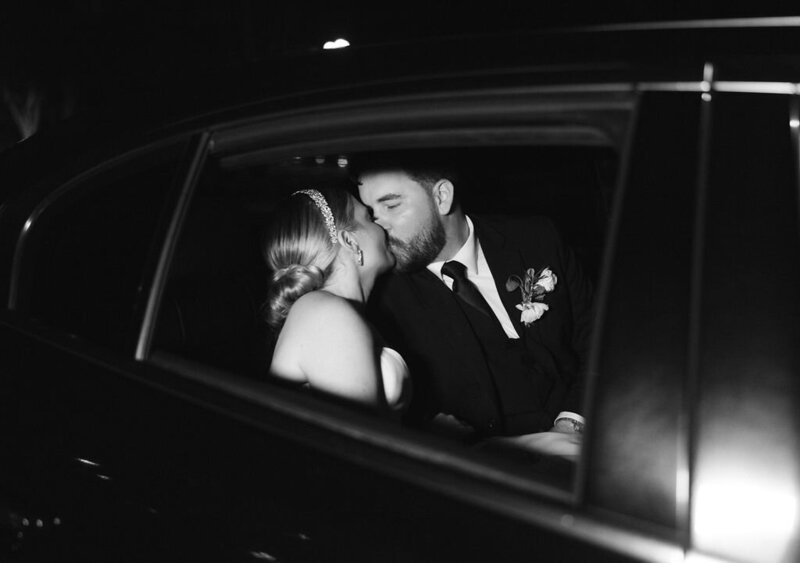 Bride and groom kissing in car after wedding exit