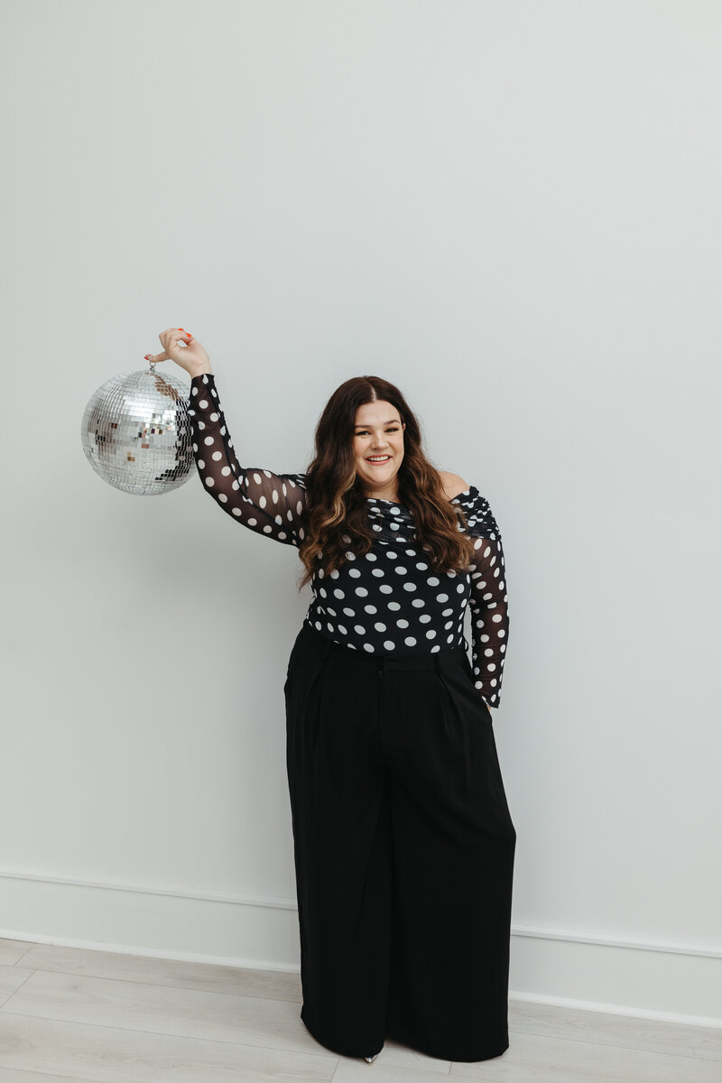 Woman in polka dot shirt and black pants holding a disco ball