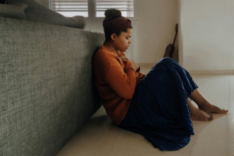 Woman sitting on floor with eyes closed leaning against a sofa. Photo by Joice Kelly from Unsplash