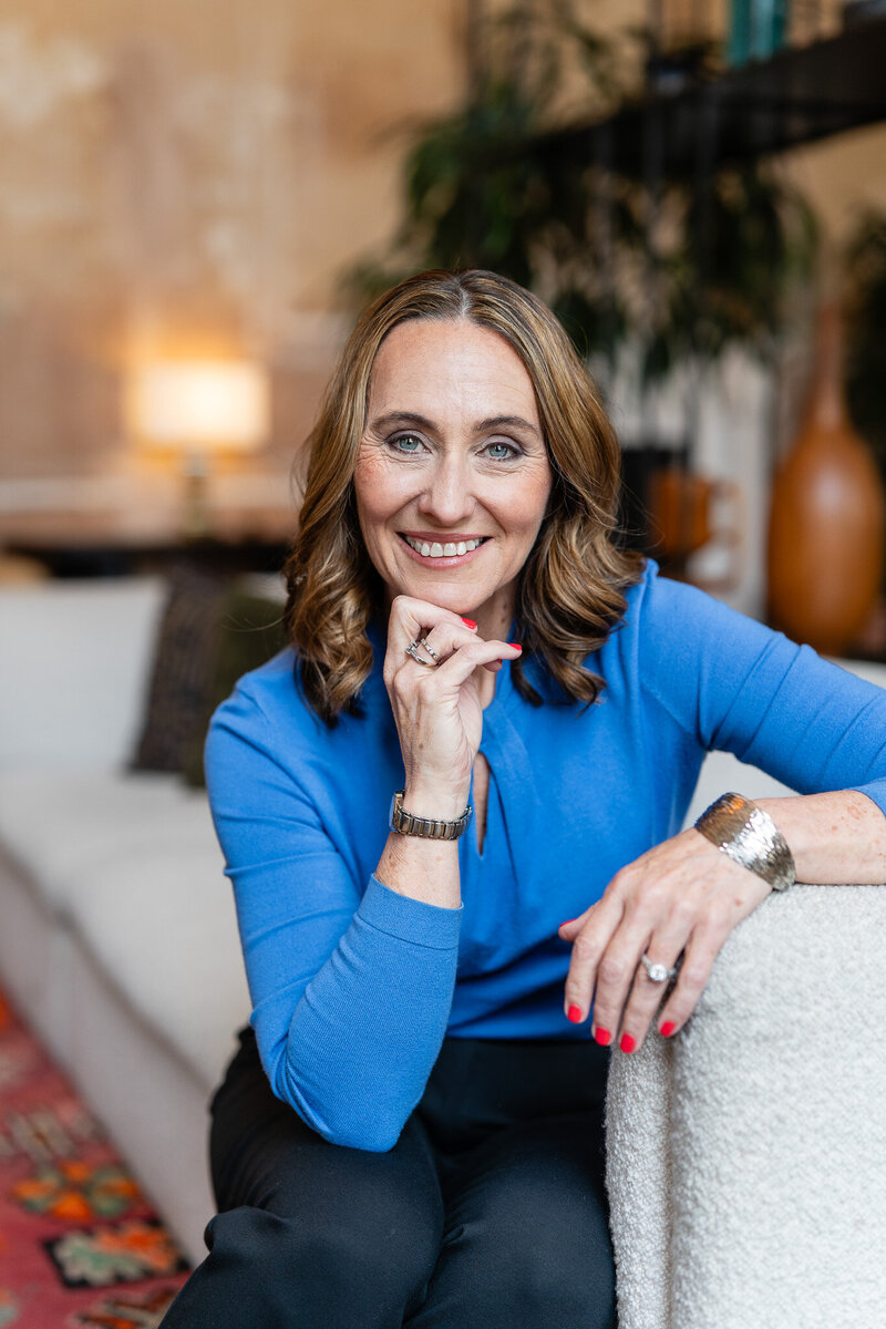 woman sitting on a soffa, wearing blue shirt and smiling to a camera
