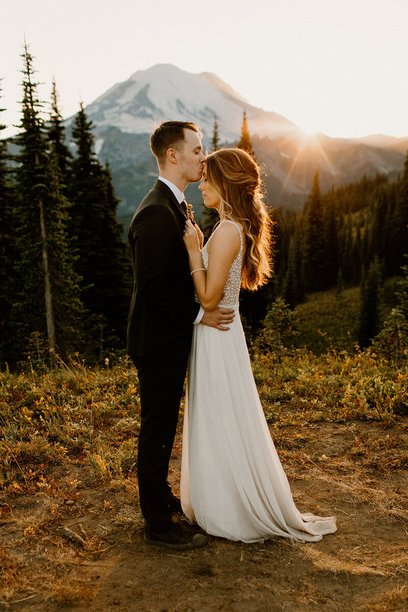 Groom kissing bride's forehead in front of Mount Rainier after elopement ceremony!